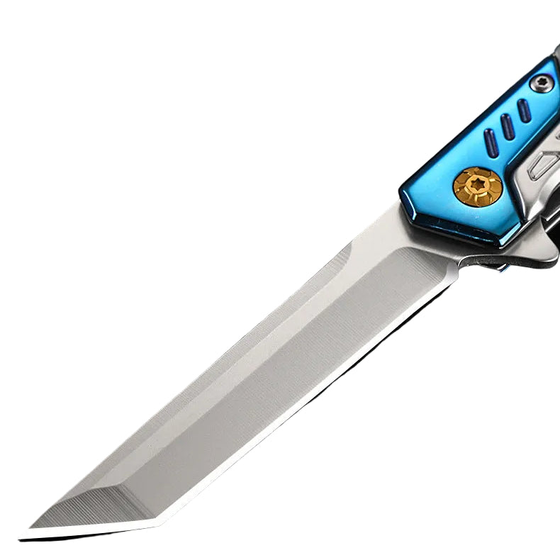 A close-up product shot of a folding knife with a satin-finished silver blade and a metallic blue handle featuring a gold accent, resting on a dark reflective surface next to a black textured case. Chinese text is visible in the upper left.